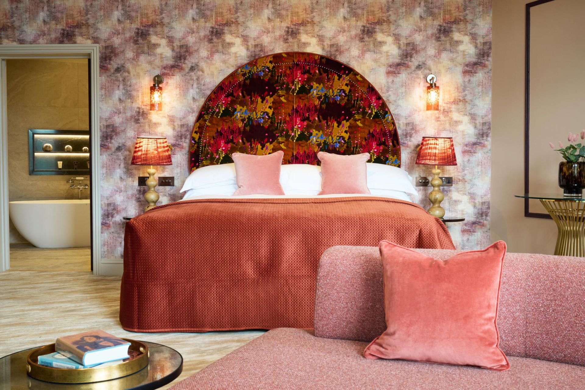 Hotel bedroom with floral wallpaper, pink velvet seating and a rose pink bedpsread