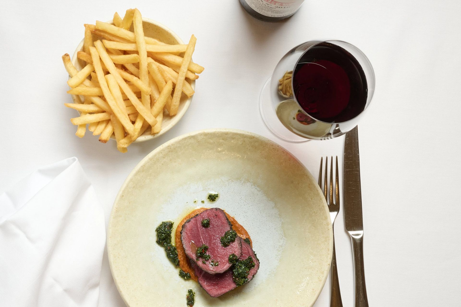 Aerial view of venison dish with French fries and a glass of red wine