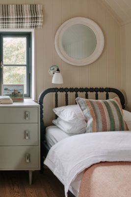 Cream kids' bedroom with black wrought iron bedframes, pastel pink bedspreads and a cream chest of drawers