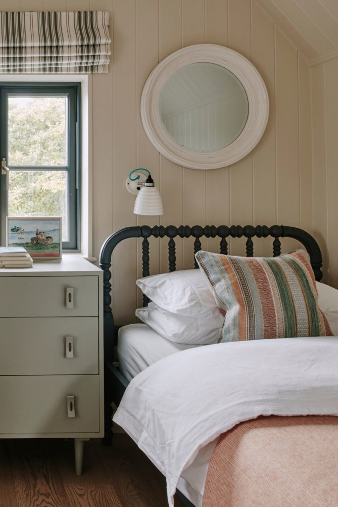 Cream kids' bedroom with black wrought iron bedframes, pastel pink bedspreads and a cream chest of drawers