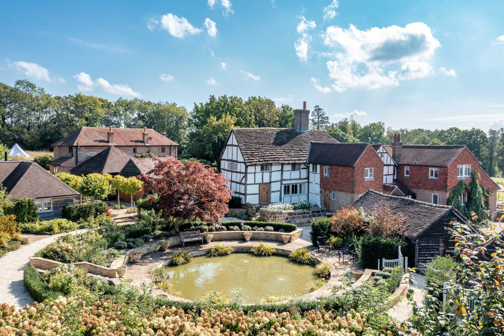 Aerial view of farmhouse with circular pond, wildflower meadow and red brick annexe