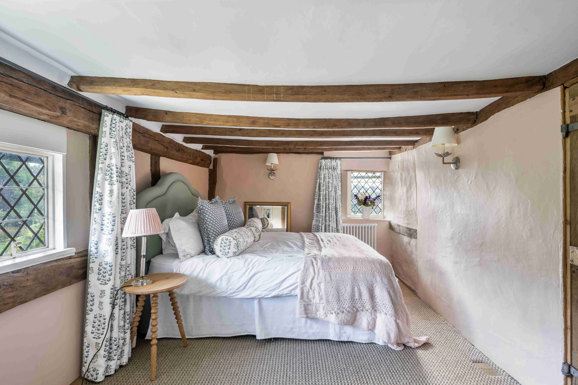 Bedroom with wooden ceiling beams, leaded windows and pale pink walls