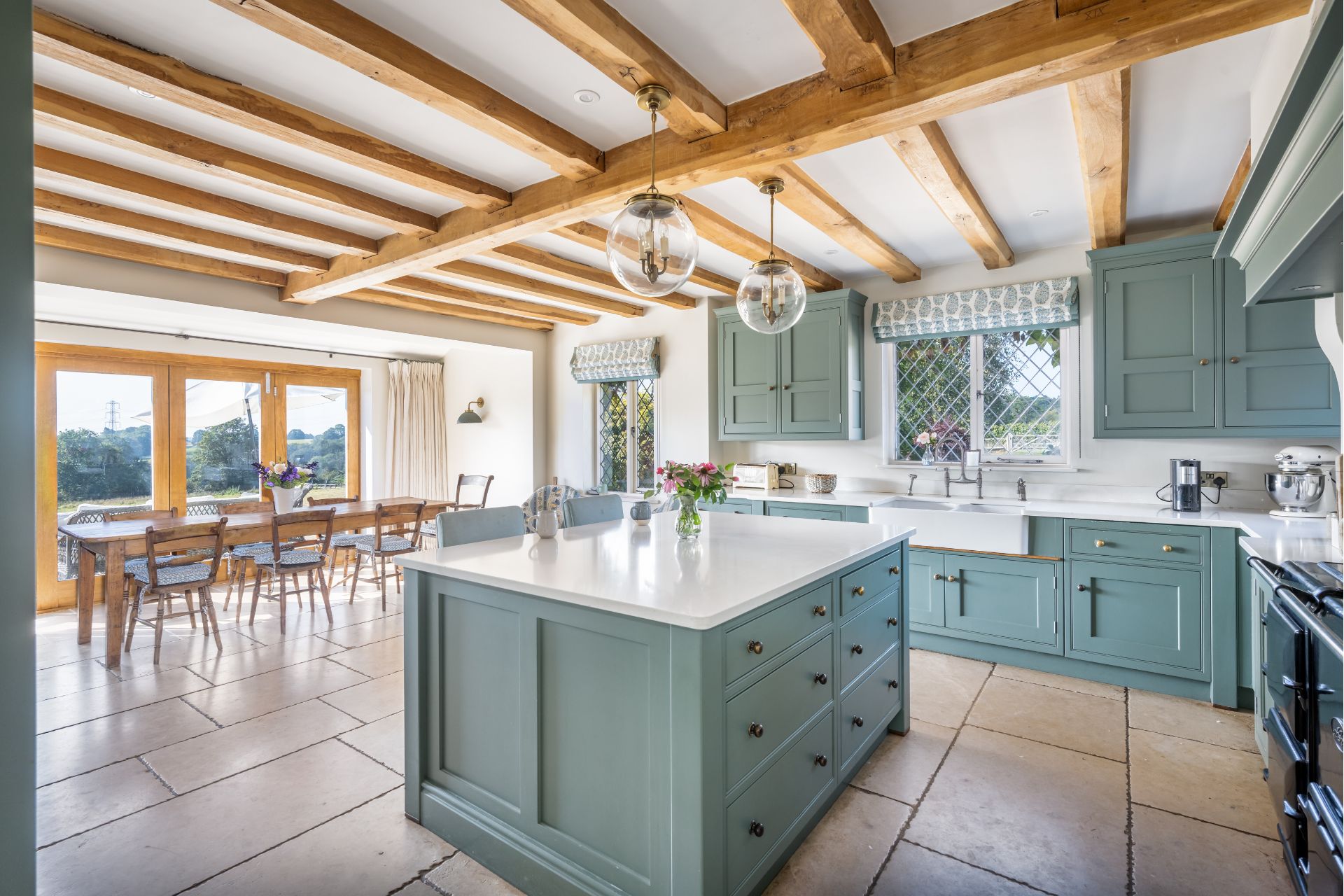 Country kitchen with teal cabinets, white worktops and wooden ceiling beams