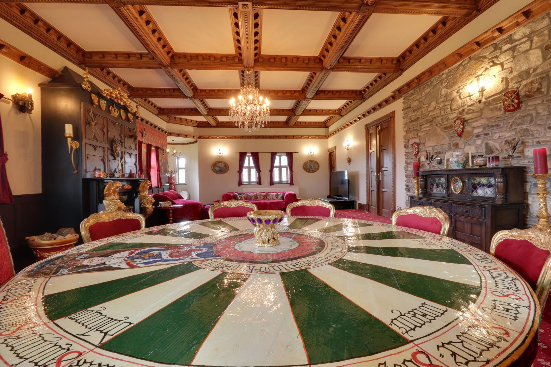 Castle living room with panelled ceiling, chandelier and King Arthur roundtable surrounded by red velvet seats