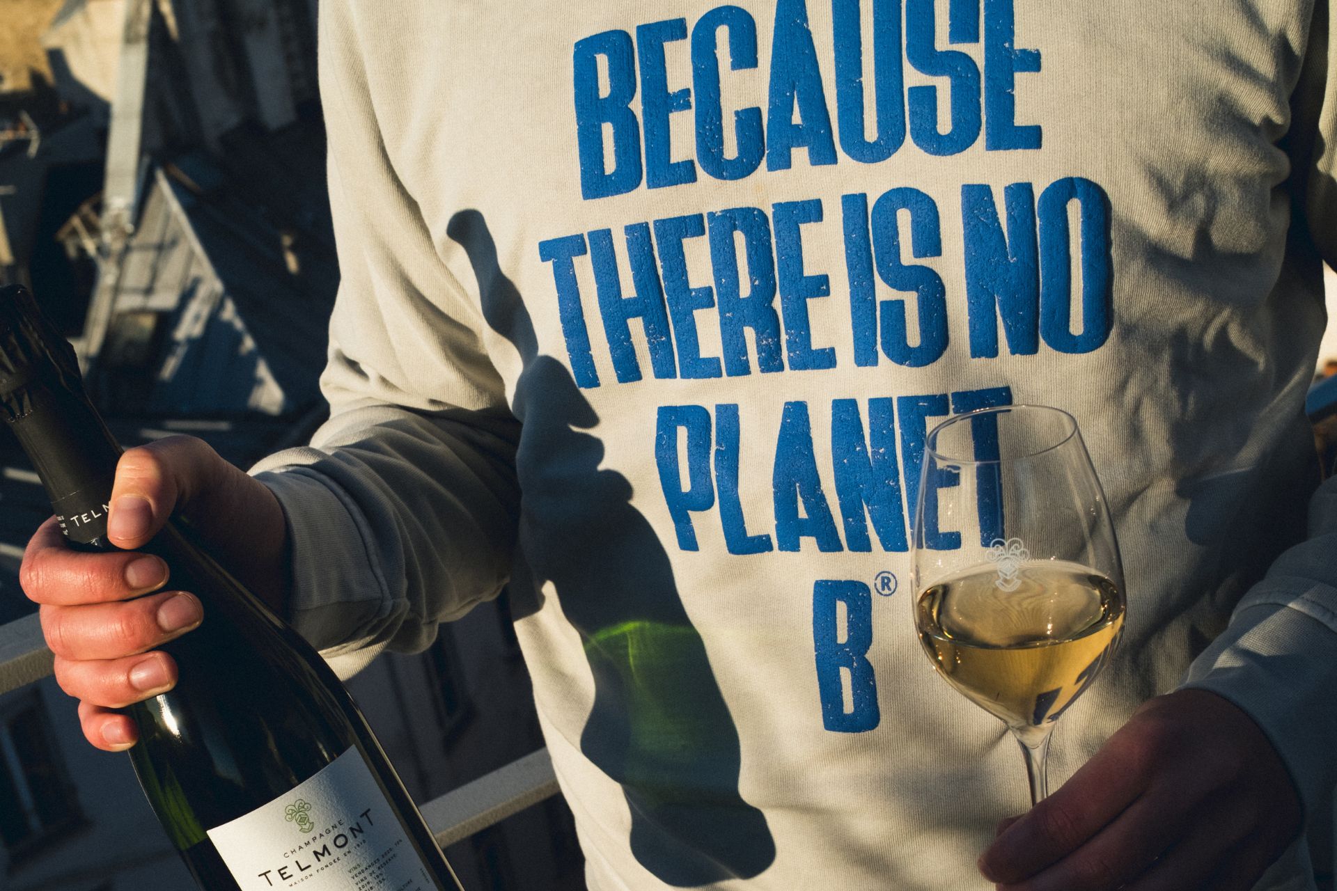 Man holding Telmont champagne, wearing a white sweatshirt printed with the words 'Because there is no planet B'