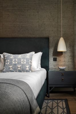 Bedroom with dark grey textured wallpaper and white bedsheets with a light grey bedspread.