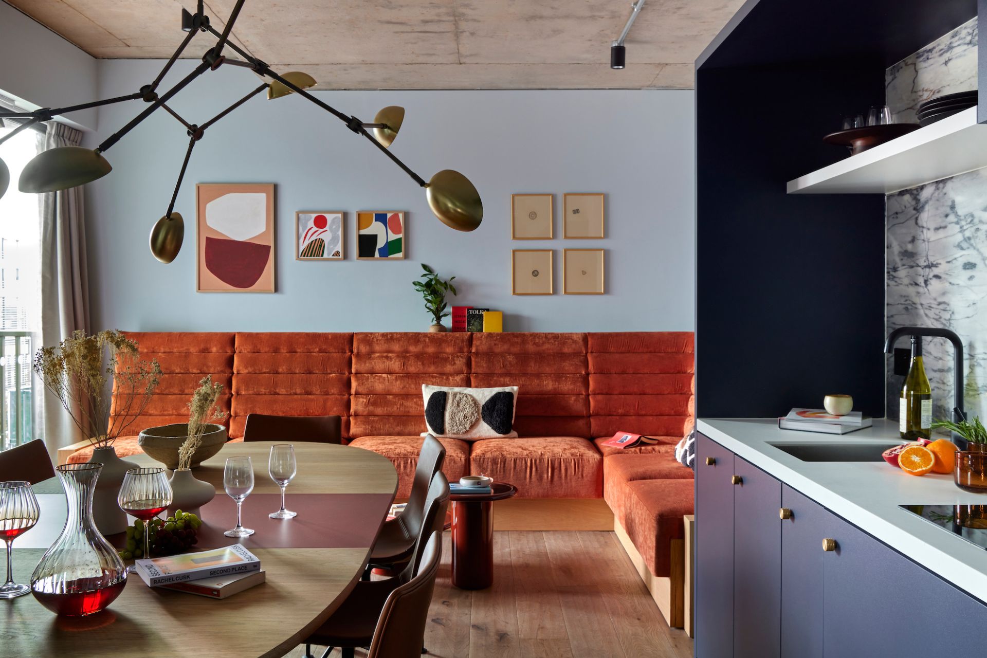 Kitchen with navy cabinets, a dark wooden dining tanle and pale blue walls with an orange velvet sofa.