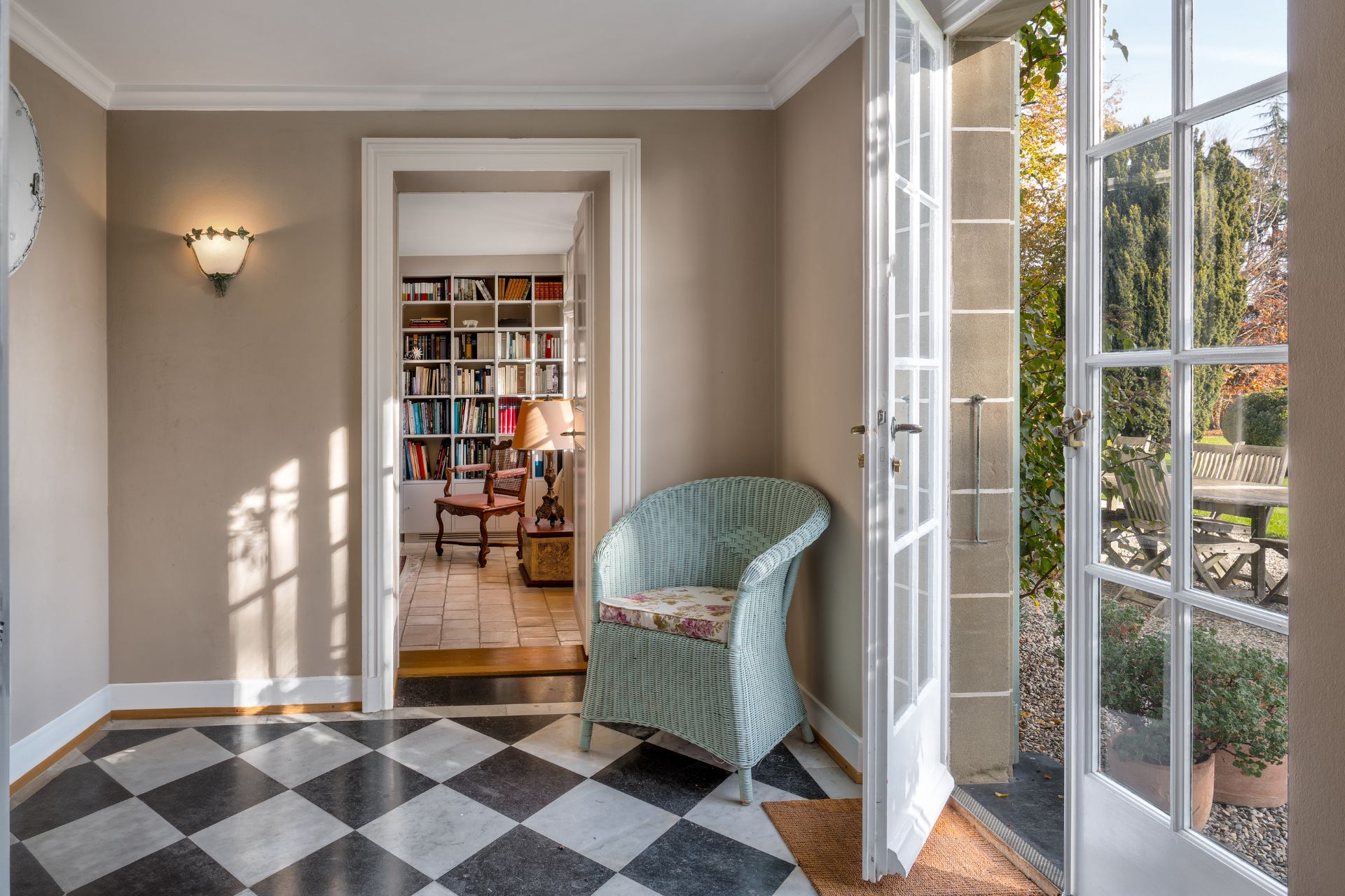Hallway with black and white diamond flooring, a pale blue armchair and French doors.