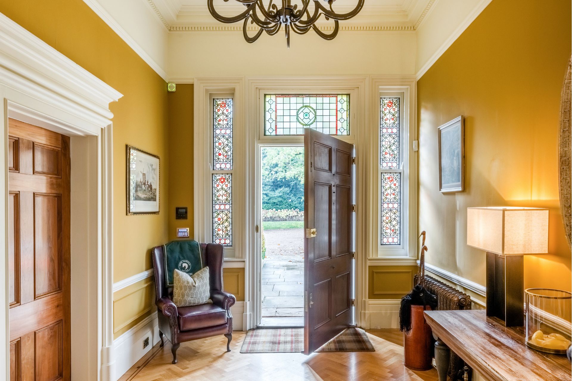 Country home entrance hall with stained glass windows, oak herringbone floors, mustard-yellow walls, and leather armchairs