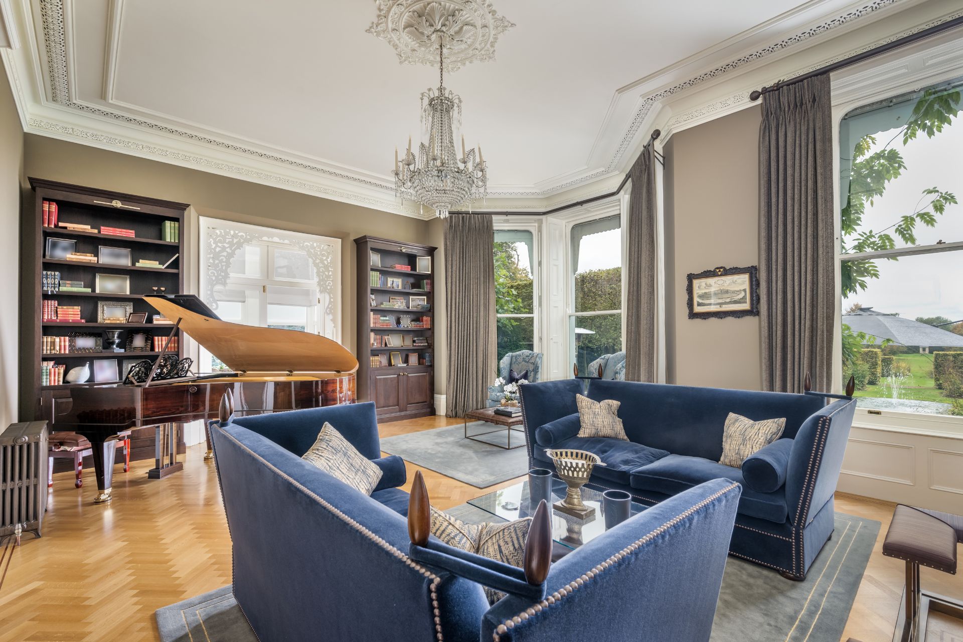 Living room with ceiling cornicing, a crystal chandelier, blue velvet sofas and a grand piano