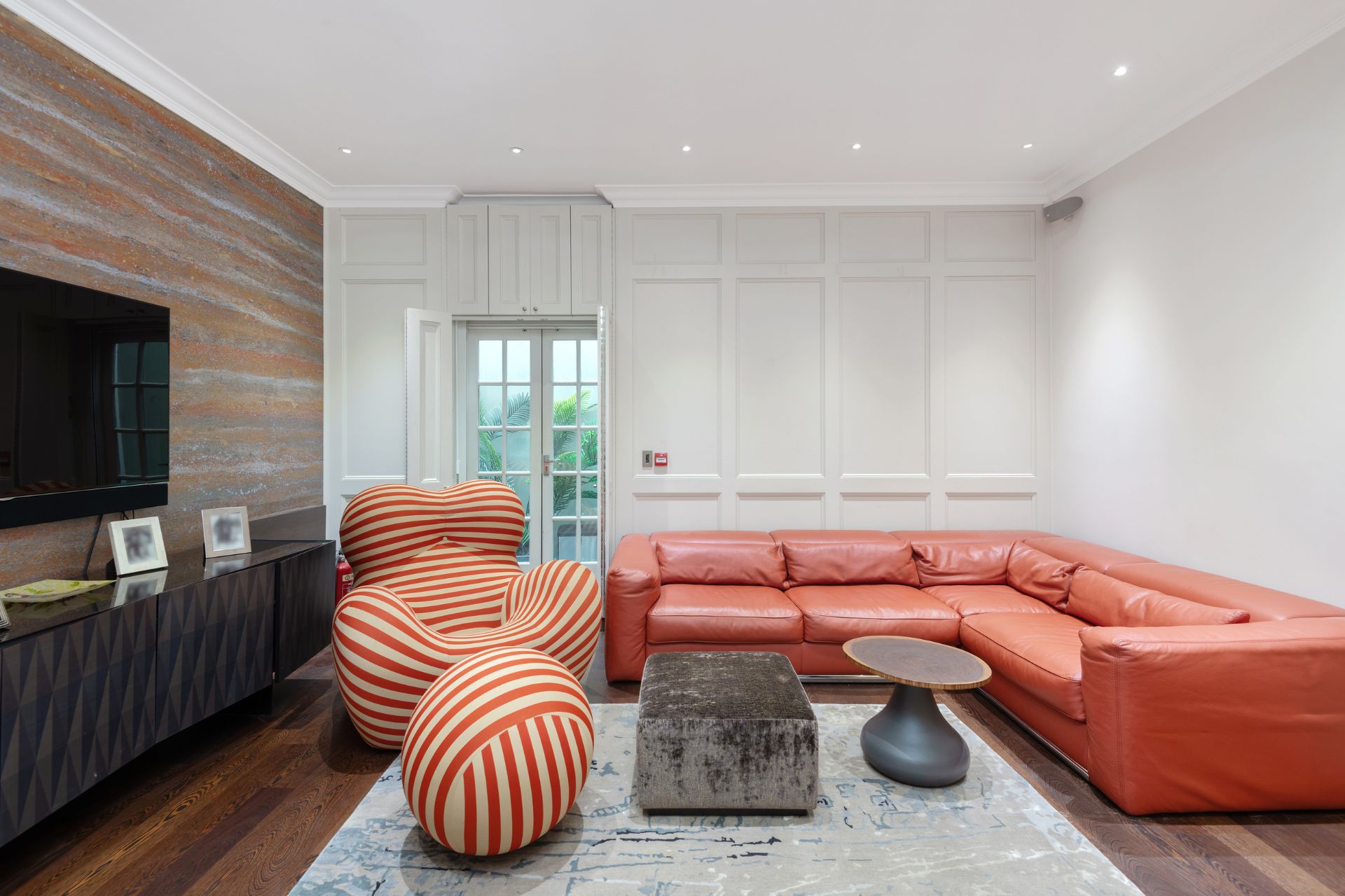 Living room with red leather corner sofa, red designer chairs and cream rugs.