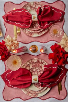 Aerial view of Valentine's table with pink and red scalloped placemats, red and white scalloped napkins, heart napkin rings and burgundy and white patterned dishes.