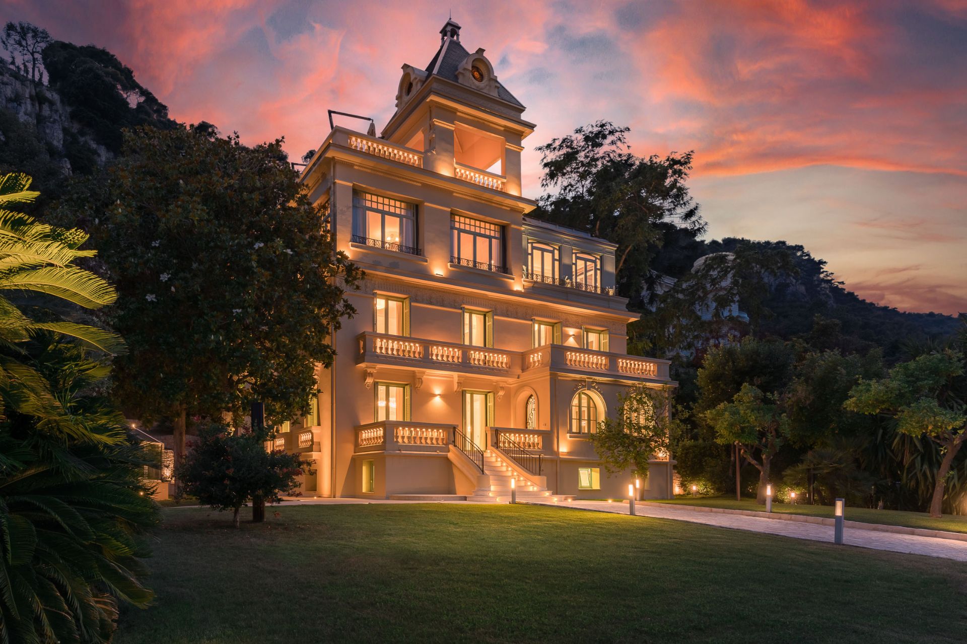Large Bello Epoque-style villa with a sweeping lawn, photographed at twilight.
