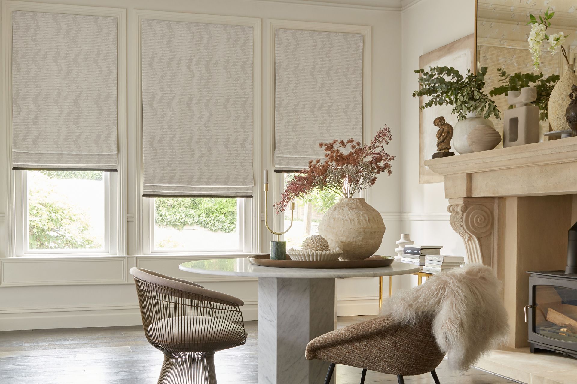 Dining room with cream walls, cream patterned blinds, a marble table and curved chairs.