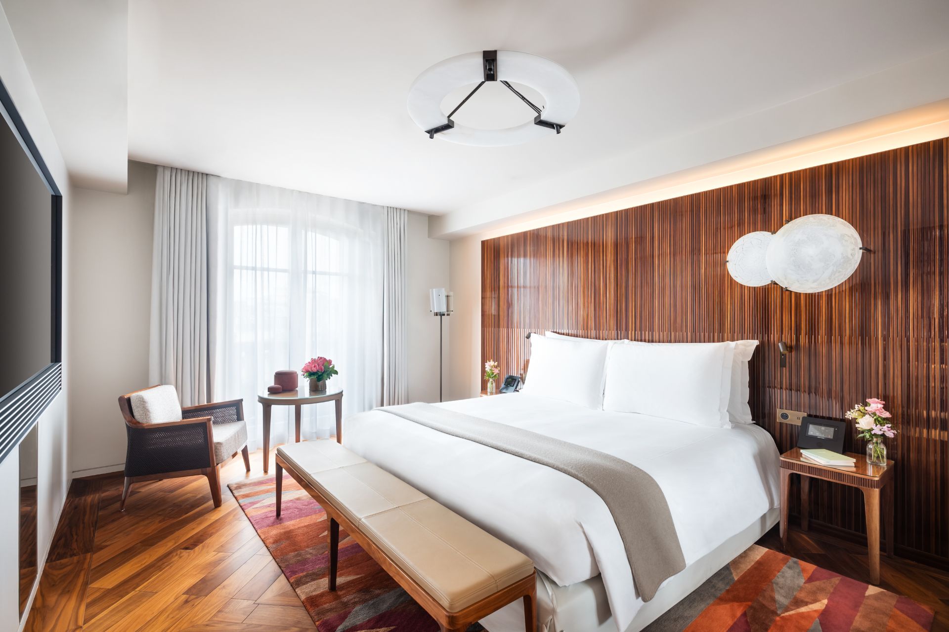 Bedroom with wood-panelled feature wall, white bedding and a beige leather chaise longue