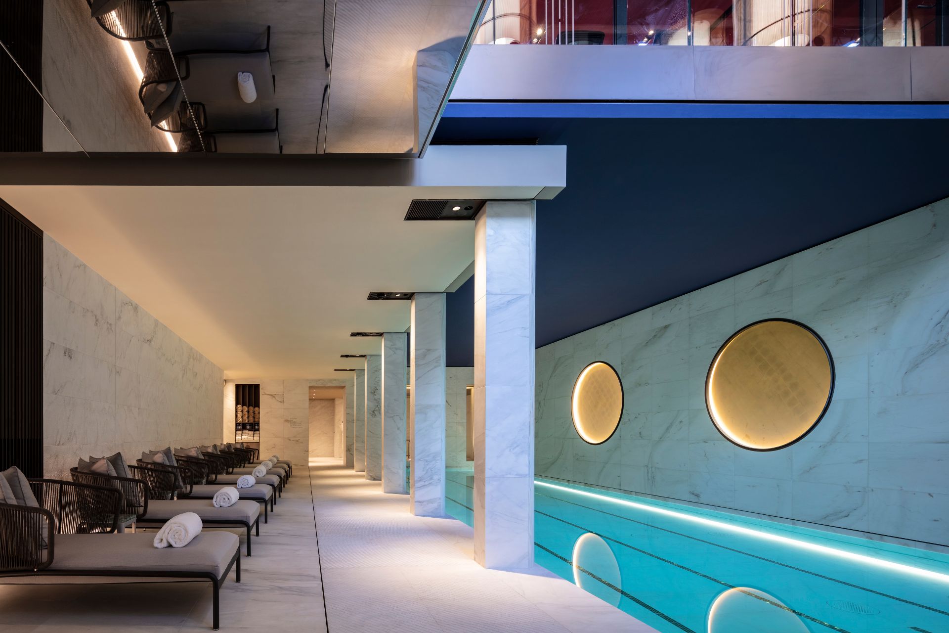 Hotel pool with cream sun loungers, white marble walls and circular wall lights