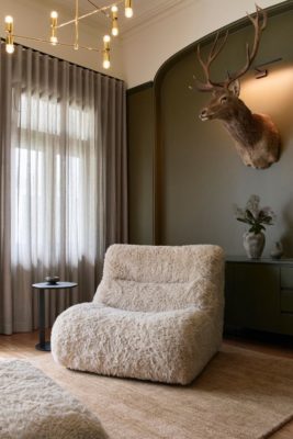 Living room with fluffy cream low-slung armchair, a brown rug and a deer head on the wall.