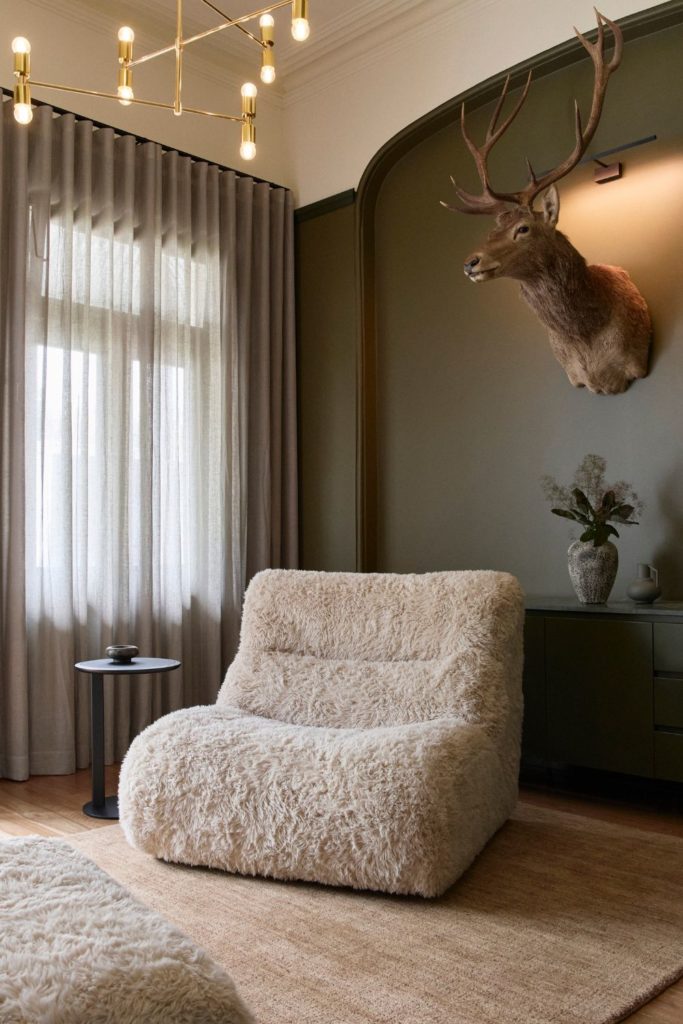 Living room with fluffy cream low-slung armchair, a brown rug and a deer head on the wall.