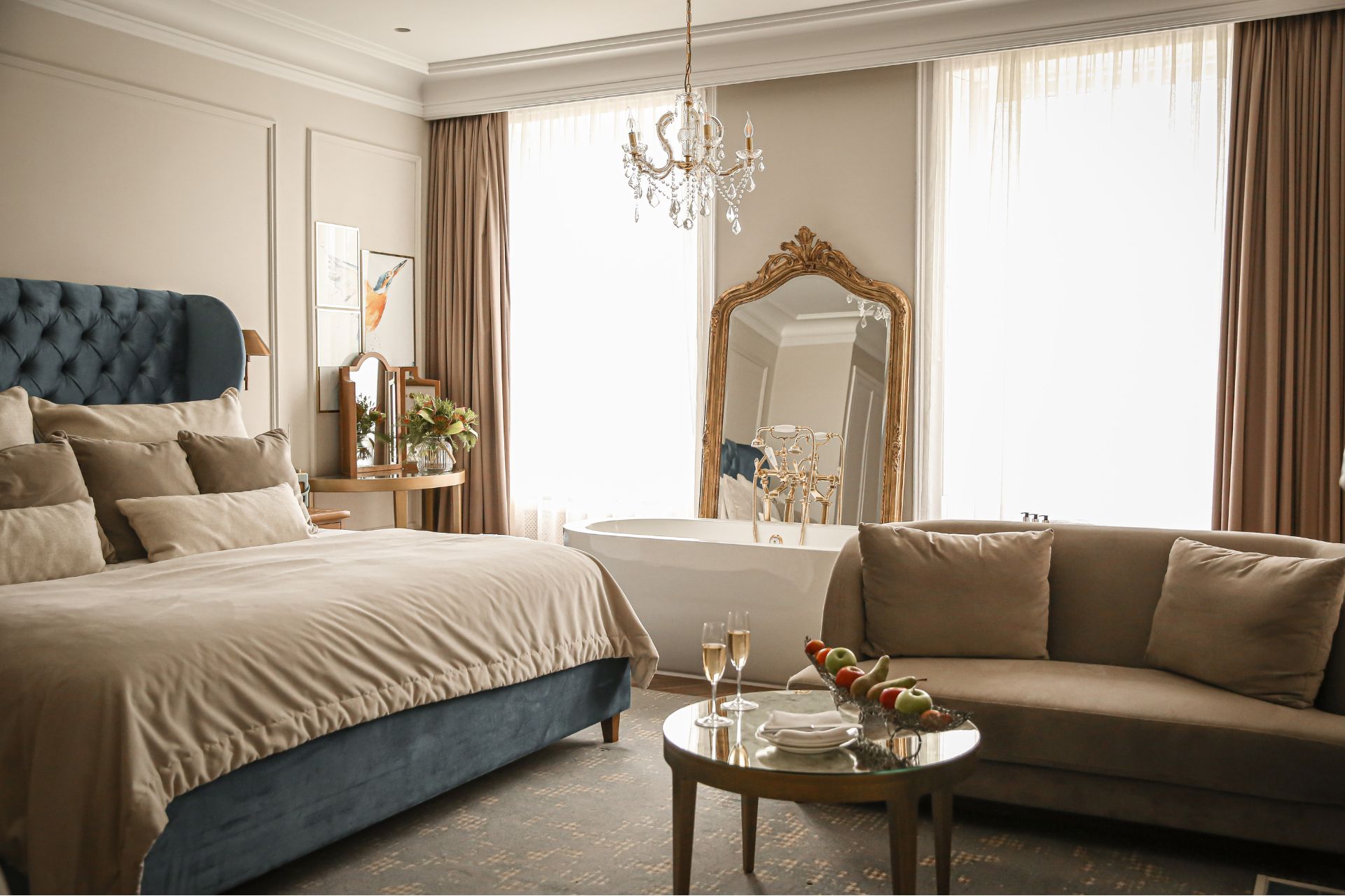 Hotel beroom with blue velvet headboard, a gilded mirror and a taupe sofa