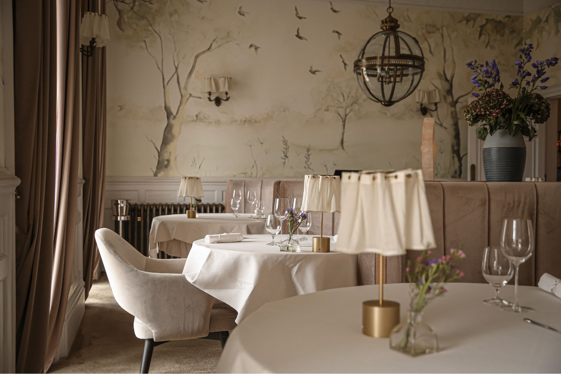 Restaurant with white tablecloths, cream armchairs and woodland motifs