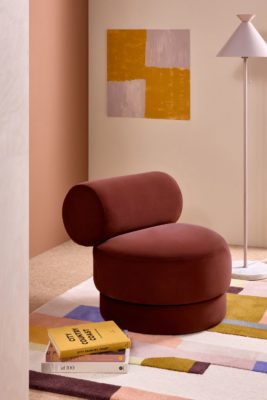 Peach-coloured room with yellow art and a modern burgundy velvet amrchair.