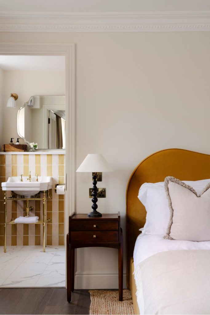 Bedroom with deep orange velvet headboard, white bedding, and an open door into a yellow and white striped en suite