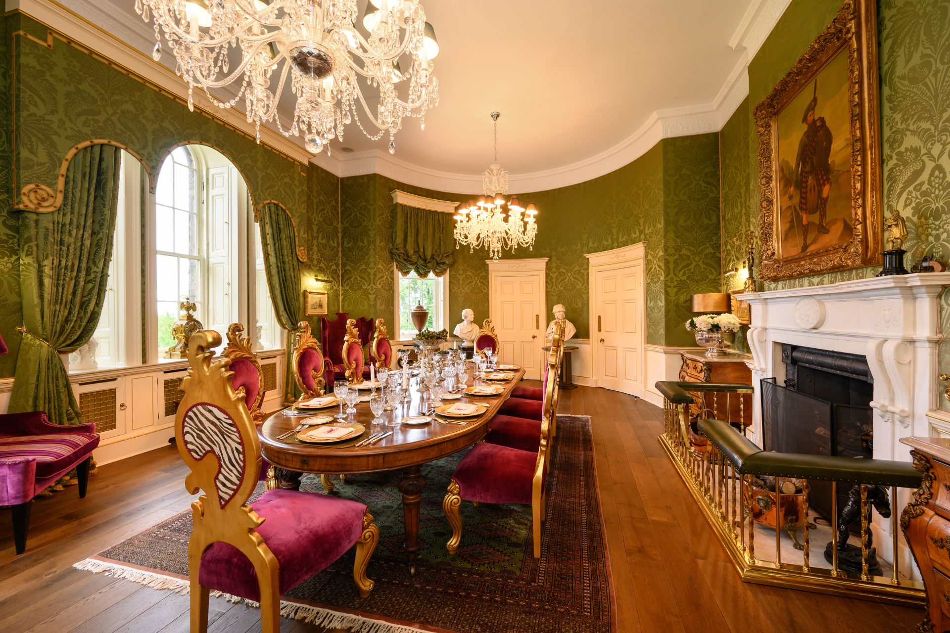 Castle dining room with moss green walls, red velvet dining chairs, oak floors and a crystal chandelier
