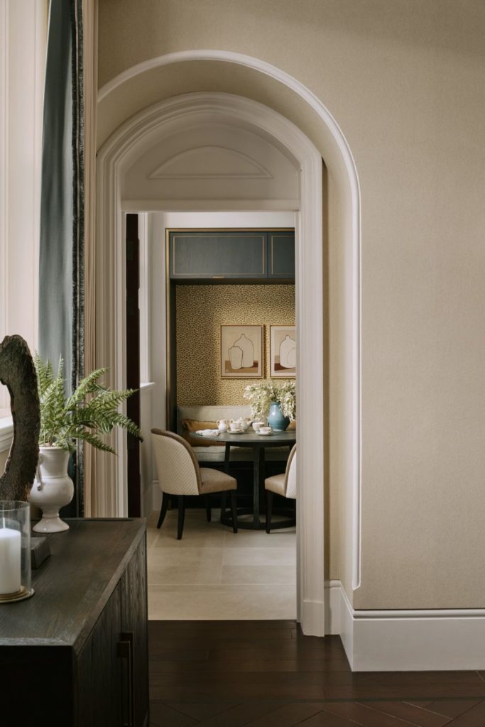 Living room with cream walls and arched doorway leading into a kitchen with dark wooden furniture and a yellow dining nook