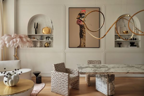 Dining room with white marble table, patterned chairs, a gold light fitting and an abstract art piece beside an arched shelf.