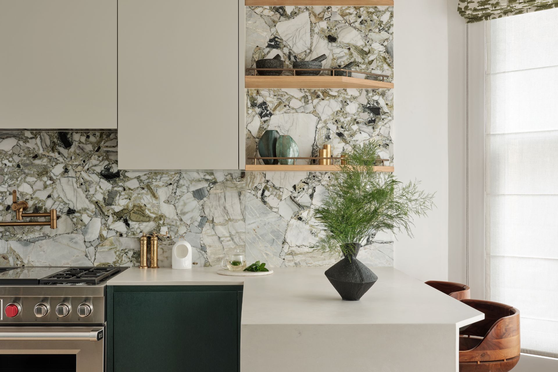 Kitchen with deep greeb cabinets, white quartzite worktops, a green and white marble splashback, and curved wooden bar stools.