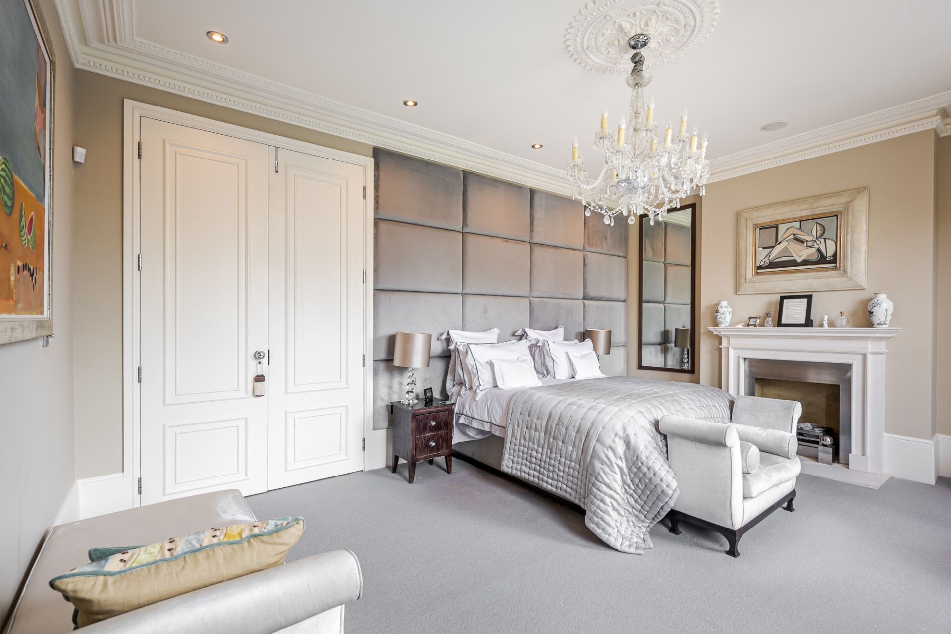 Bedroom with oversized grey headboard, white fitted wardrobes and a chandelier.