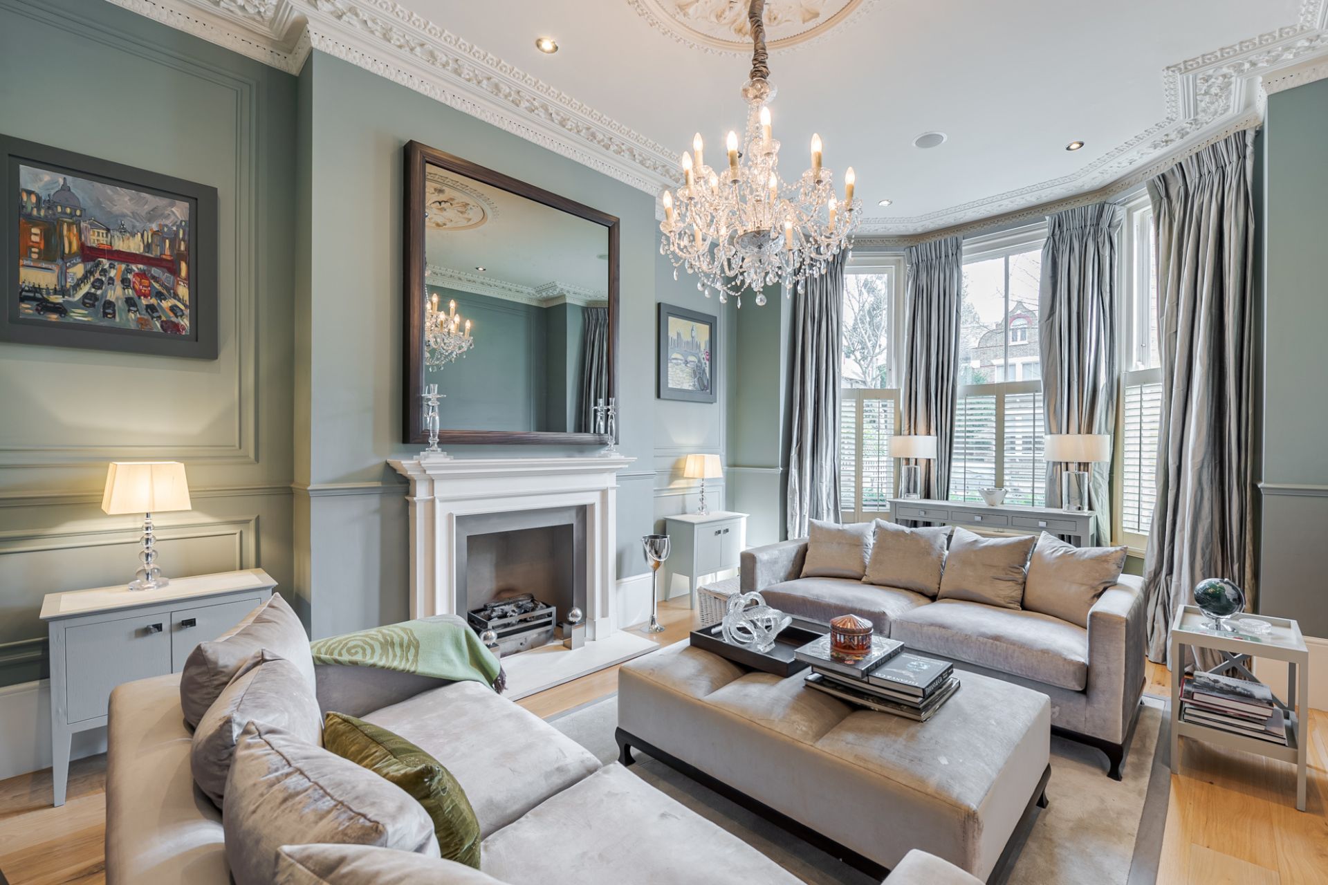 Drawing room with double height ceilings, sash windows, pale blue walls, cream sofas and a chandelier.