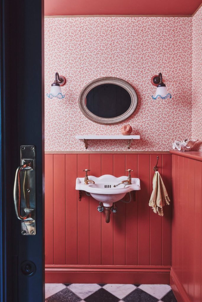 Powder room with pink floral wallpaper, red wooden panelling and black and white diamond tiles.