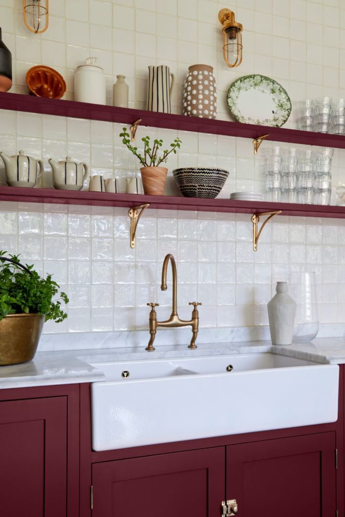 Cherry red Shaker kitchen with gold hardware, exposed shelves and a butler sink.