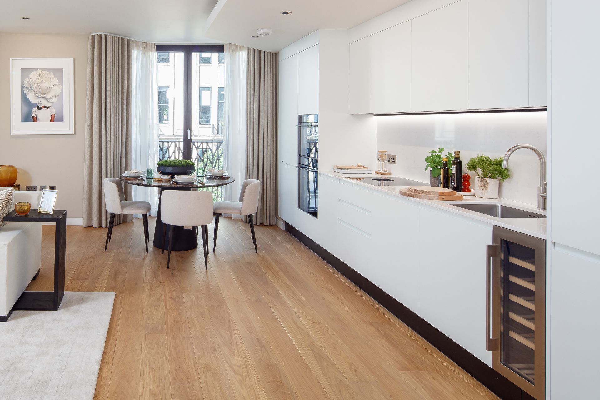 Open plan kitchen with pale wood floors, white cabinets and cream furniture.