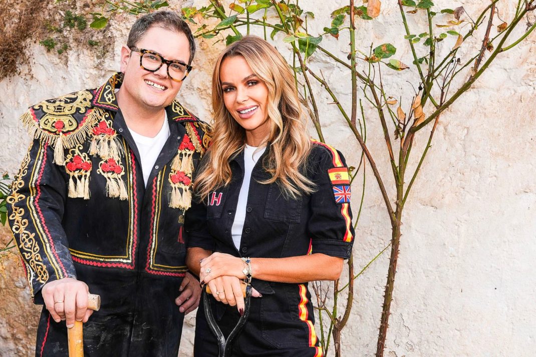 Alan Carr and Amanda Holden wearing black jumpsuits and standing outside of their renovated Spanish villa
