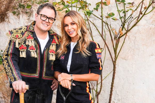 Alan Carr and Amanda Holden wearing black jumpsuits and standing outside of their renovated Spanish villa