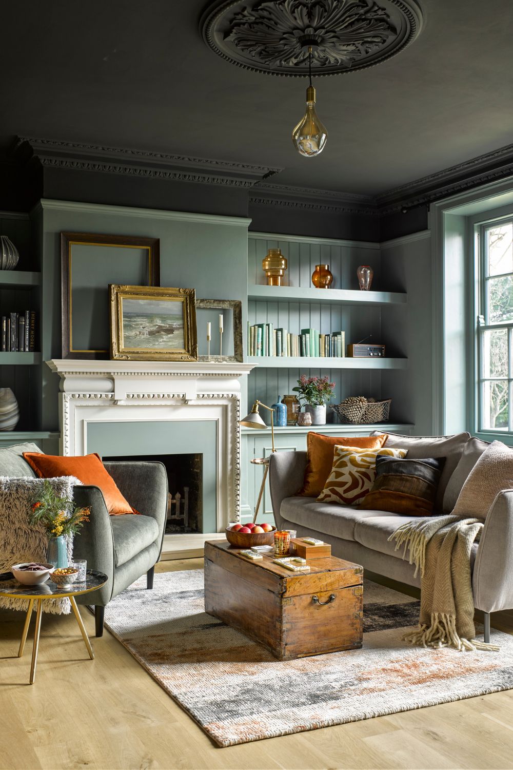 Pale blue living room with dark grey ceiling, pale grey sofas and orange accents