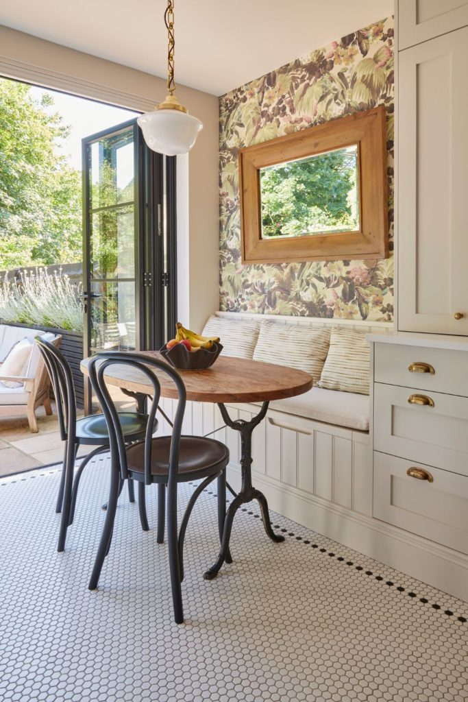 White kitchen with honeycomb tiled floor, round table, cafe chair abd integrated dining nook with floral wallpaper