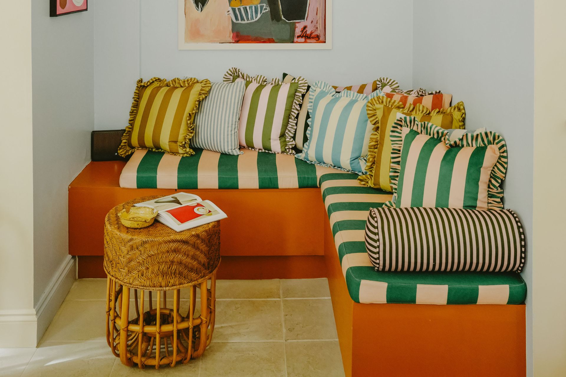 Orange banquette seat with green, pale blue, and red and yellow striped cushions with ruffles