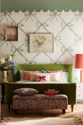 Bedroom with green bow-pattern wallpaper, green scalloped trim, a green velvet headboard and pink bow cushions