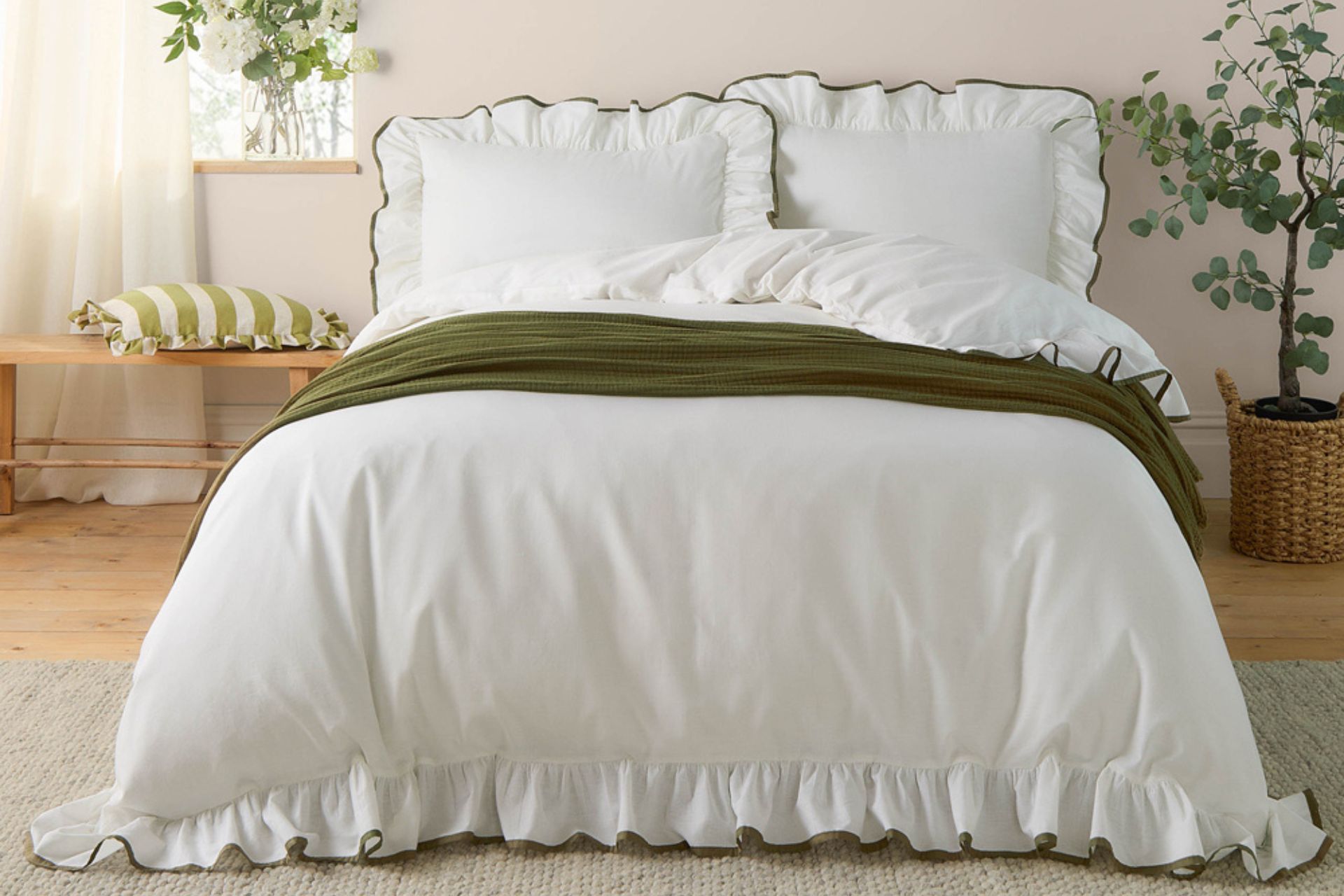 White bedding with black ruffle trim and a forest green bedspread