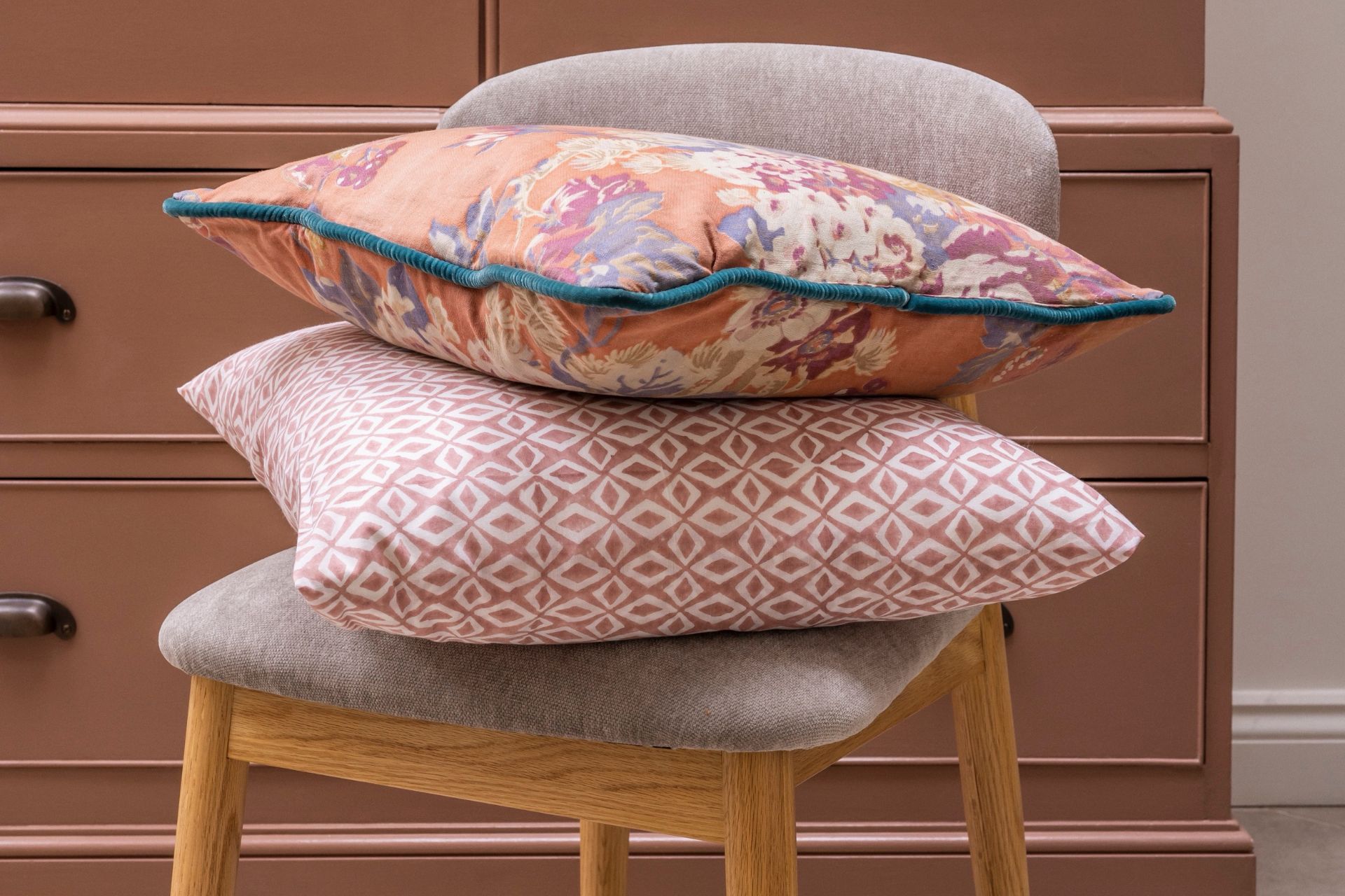 Pink and white patterned cushions on a grey chair in front of a terracotta pink wardrobe
