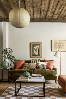 Living room with olive green velvet sofa, brown and white checkerboard rug, and coral cushions