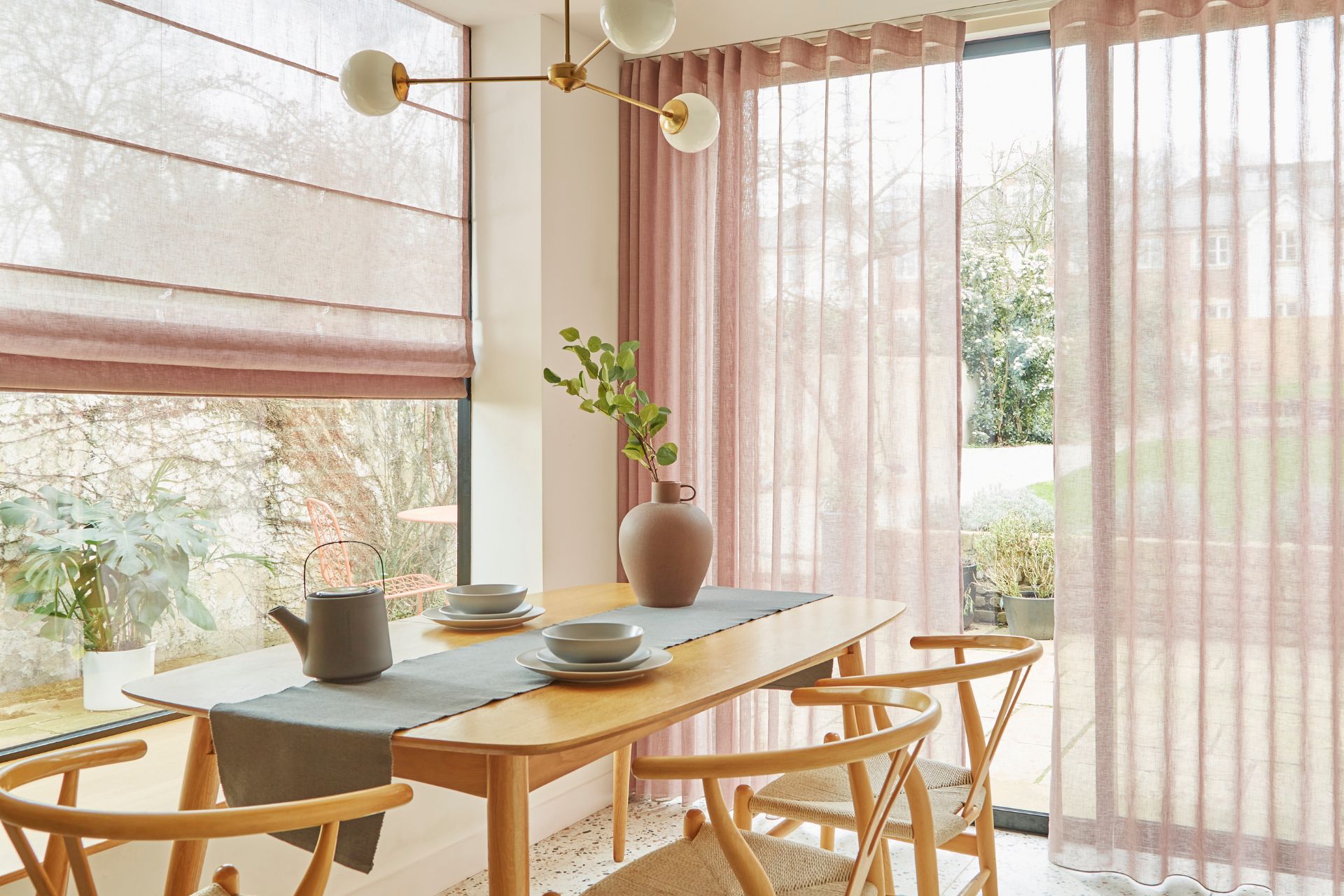 Dining room with pale oak furniture, a grey table runner, and pale pink sheer curtains.