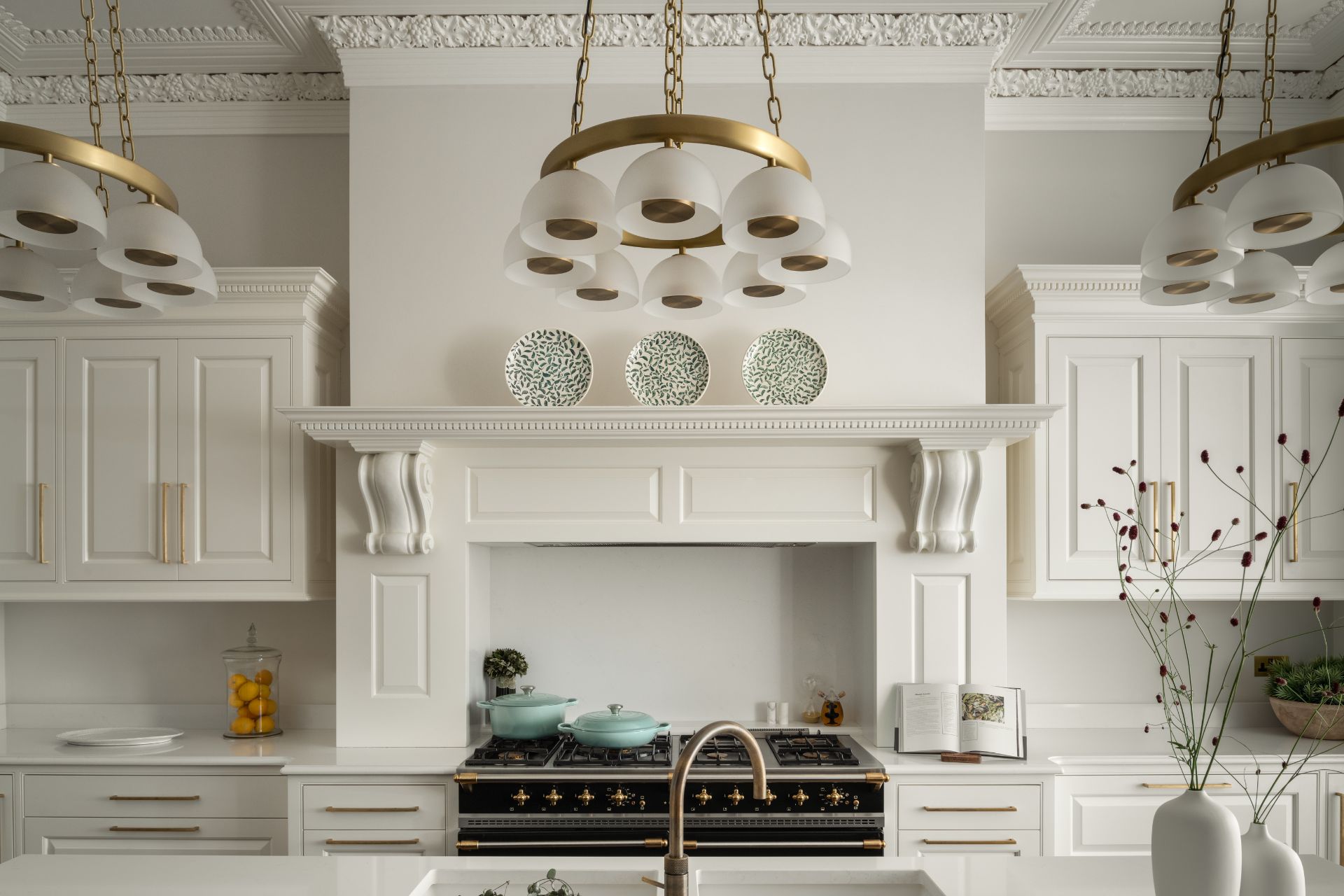 White kitchen with ceiling corning, marble worktop, a range cooker and a gold modern chandelier.