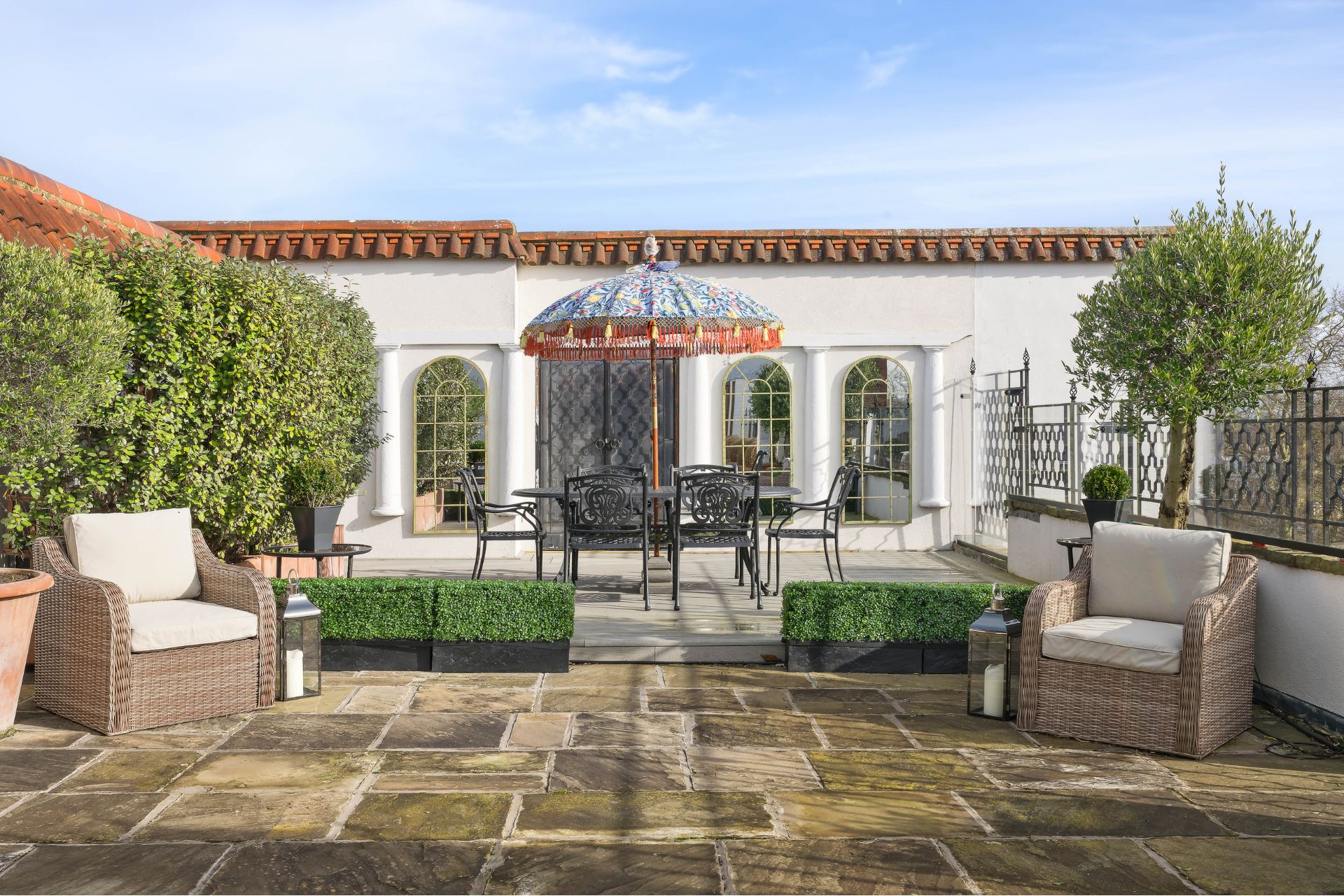 Penthouse garden with flagstone floor, cream armchairs and a patterned parasol