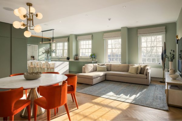 Living area with beige sofas, a grey rug, a white circilar dining table and deep orange dining chairs