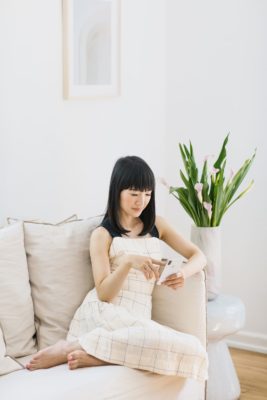 Marie Kondo wearing a white dress, sititng on a cream sofa wit a white vase of tulips beside her