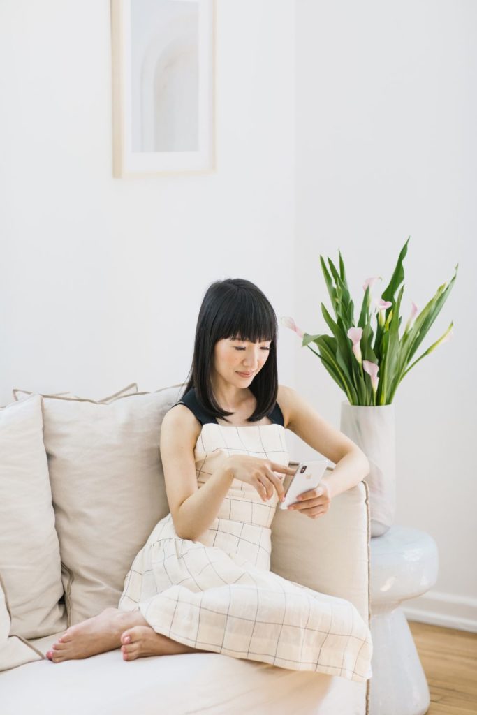 Marie Kondo wearing a white dress, sititng on a cream sofa wit a white vase of tulips beside her